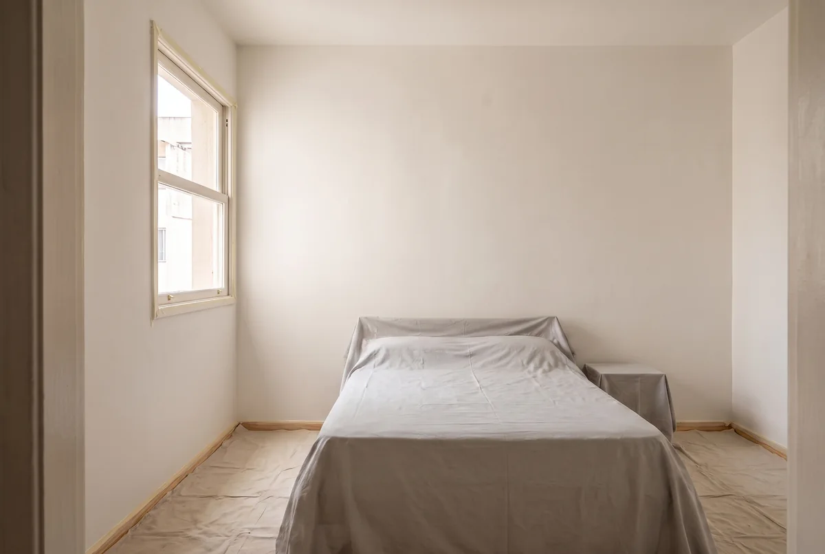 Móveis cobertos, piso protegido por lona e rodapé com fita antes de pintar o quarto.